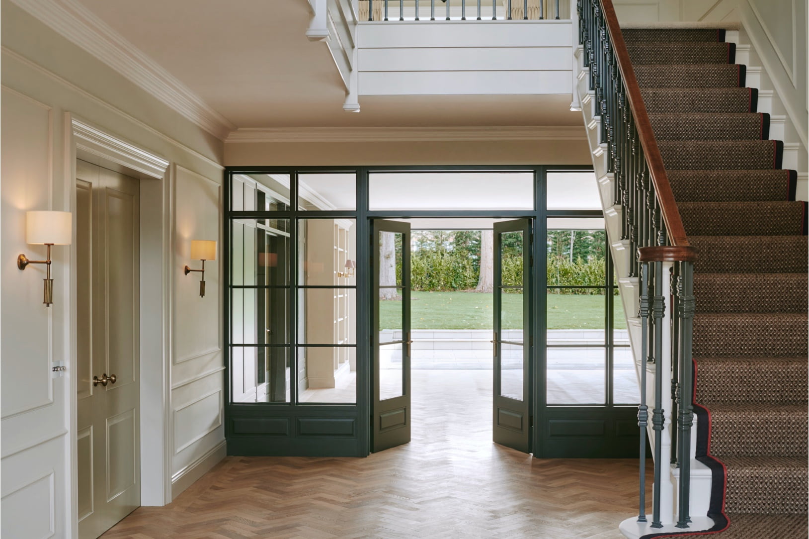 wooden floor and custom stair runner in large hallway with large doors and lots of light